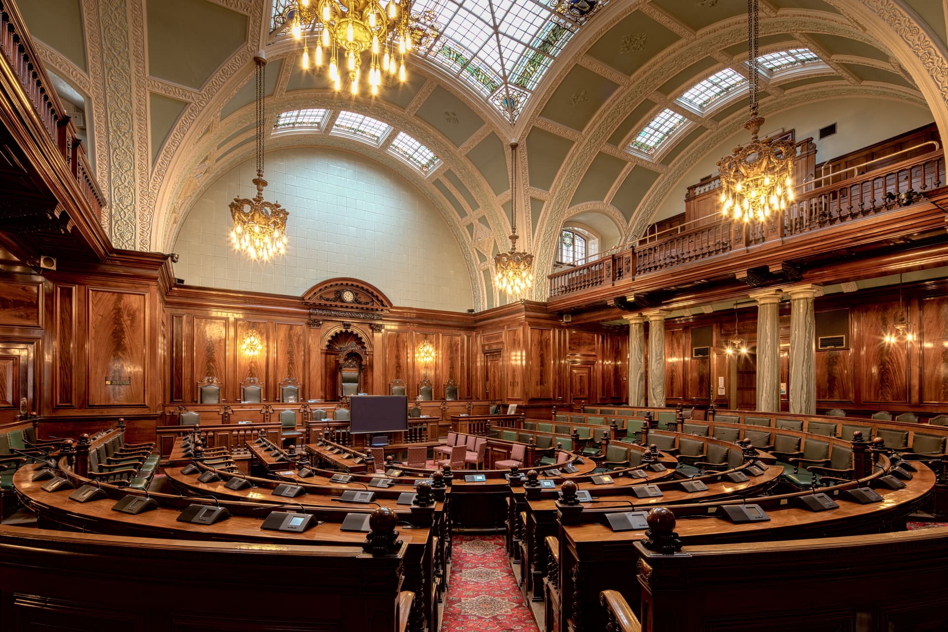 Historic wood-panelled chamber with chandeliers and a stained-glass ceiling